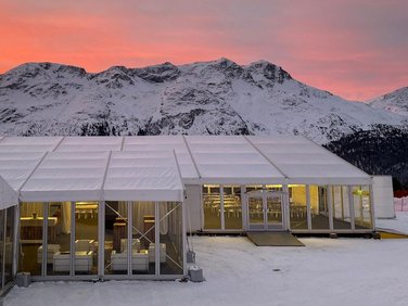 Large tent with transparent wall façade in the background mountains and red evening sky